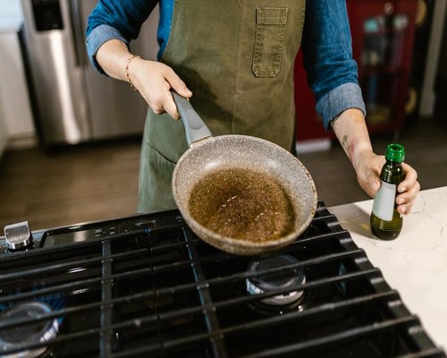 Person preparing a healthy meal with olive oil in a bright kitchen