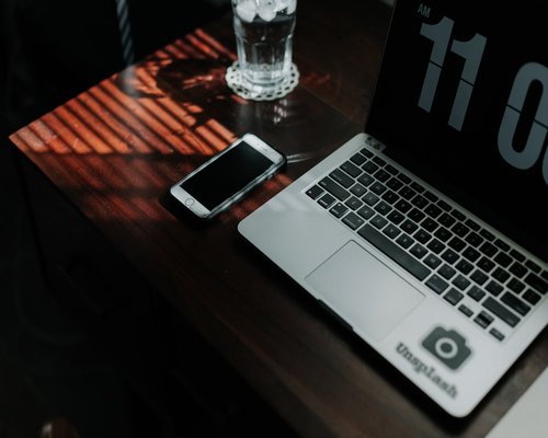 A glass of water next to a laptop and a notebook on a wooden desk